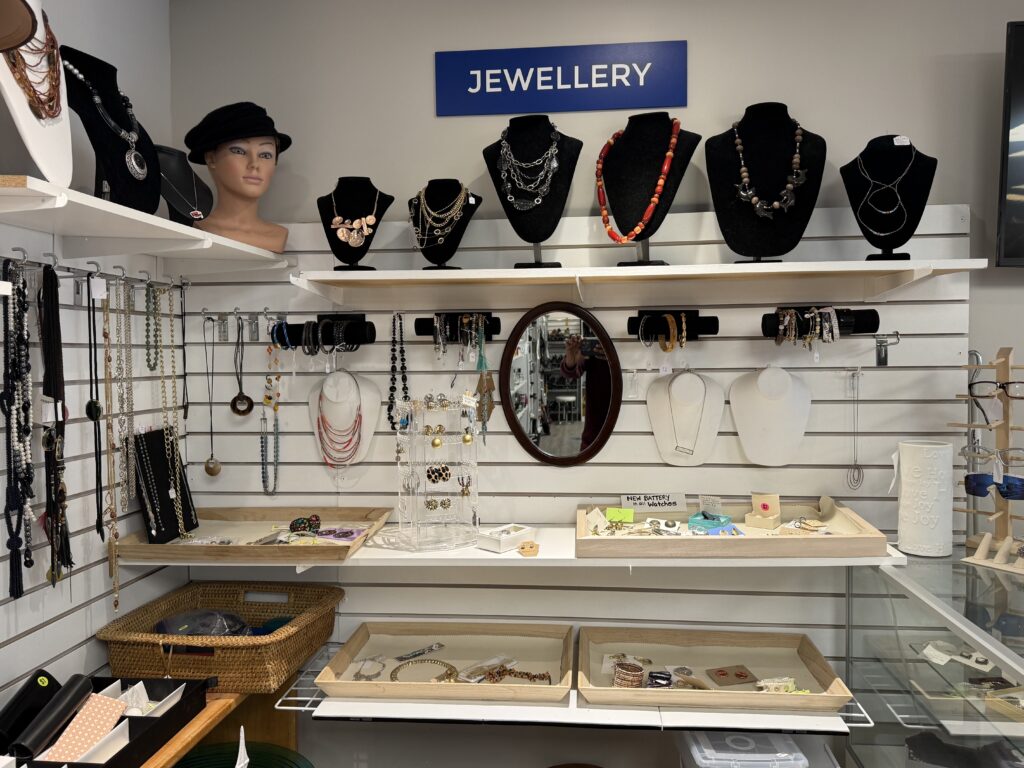 Jewelry store display with multiple necklaces on black busts beneath a blue 'JEWELLERY' sign.
